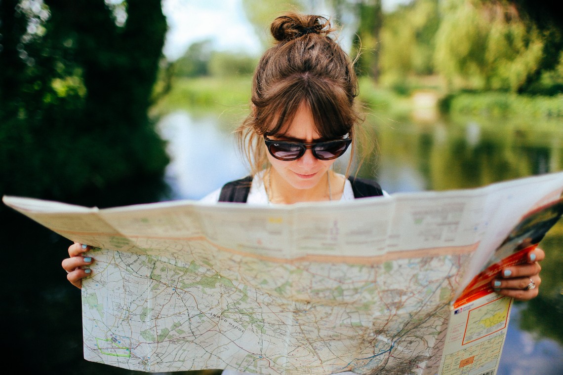 Young woman waring sunglasses reading a paper map. 